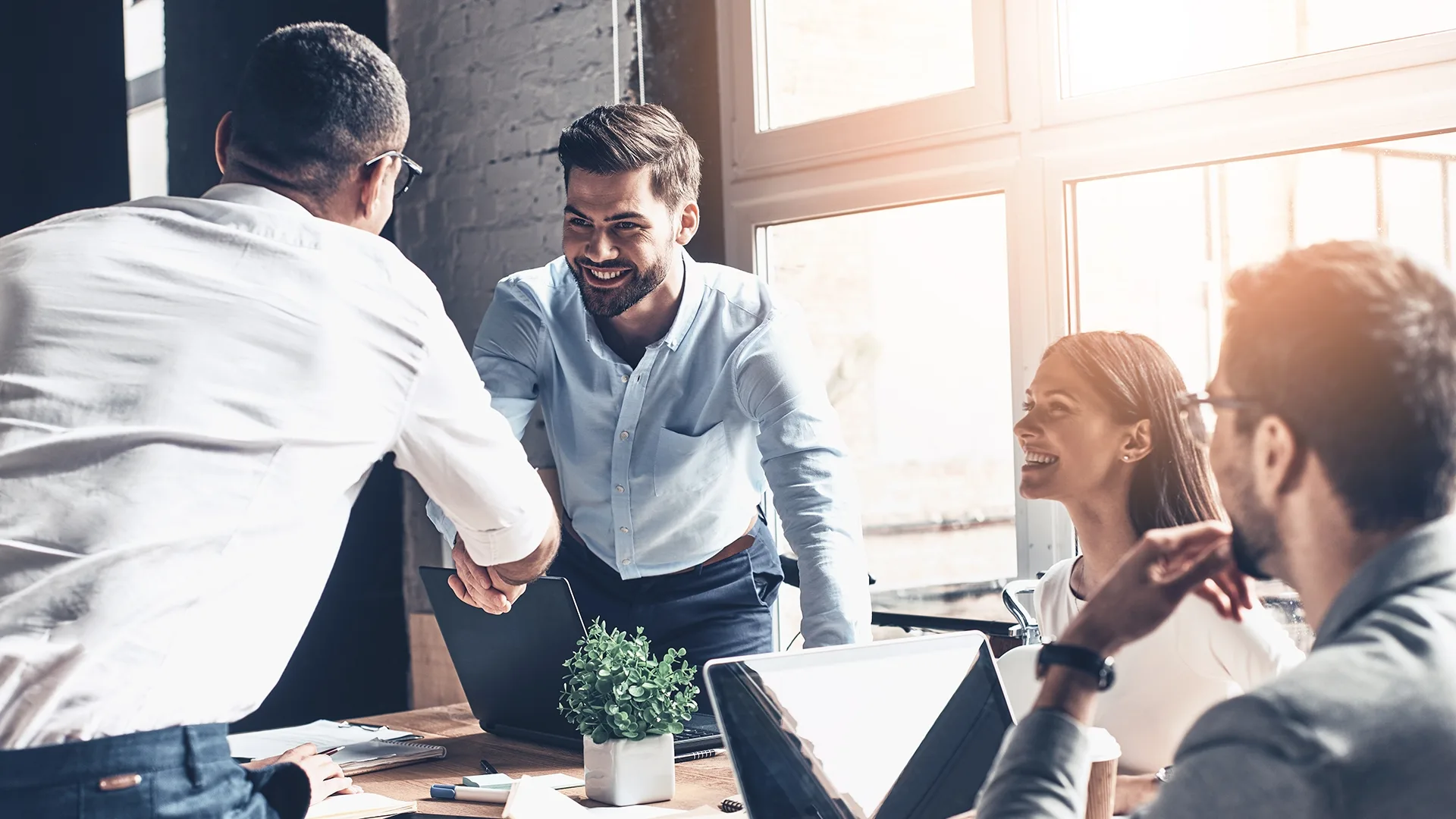 Glad to work with you! Young modern men in smart casual wear shaking hands and smiling while working in the creative office